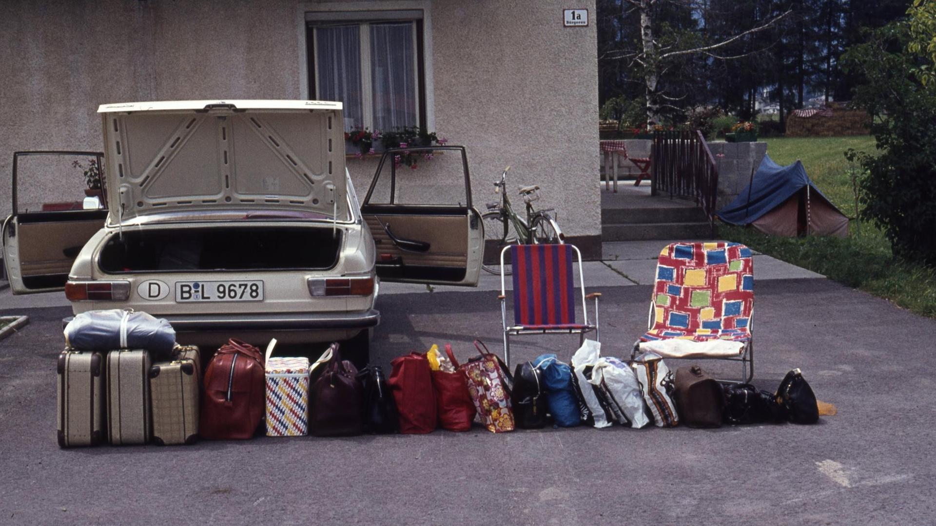 In einer Reihe stehen zahlreiche Koffer vor dem Auto.