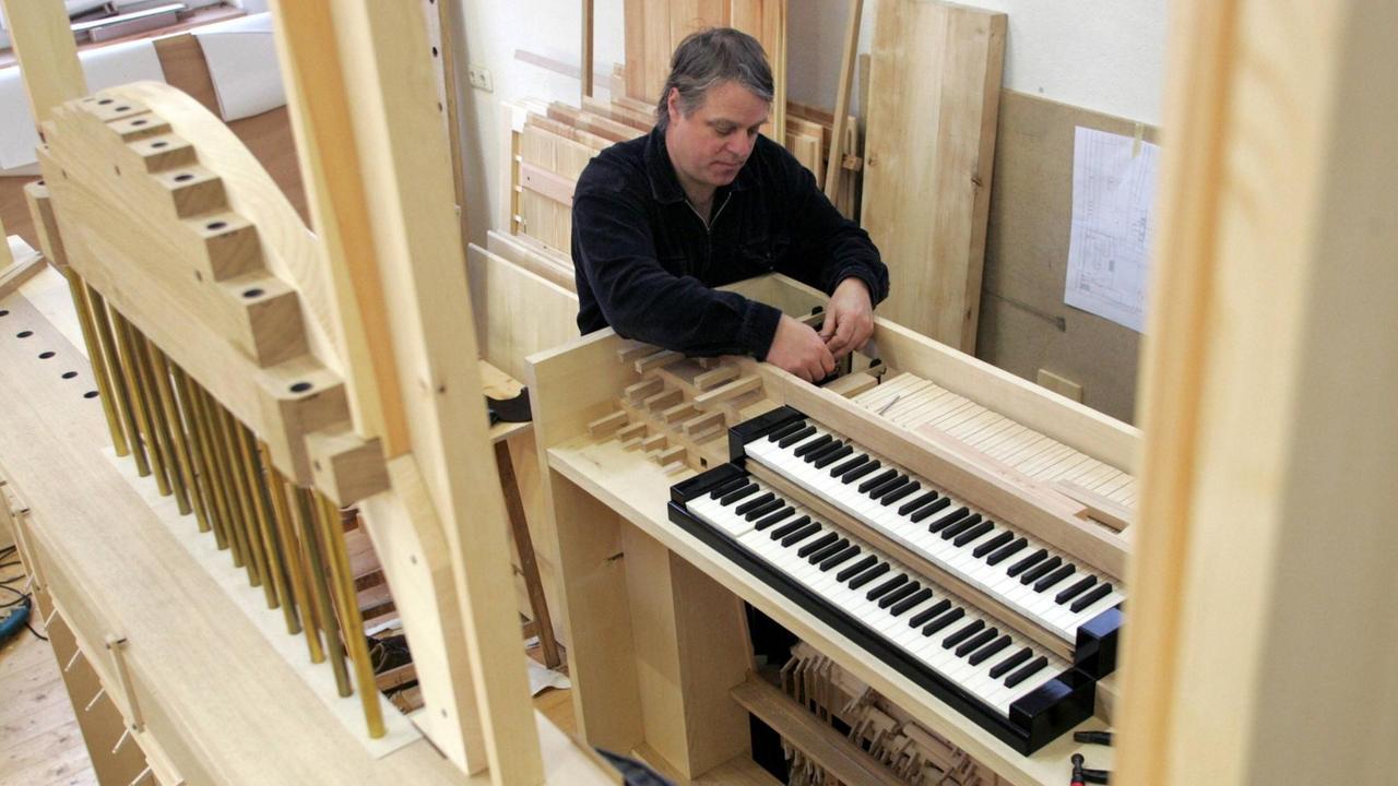 Ein Mann steht schraubend an einem Holzkasten, an dem zwei Tastaturen montiert sind.