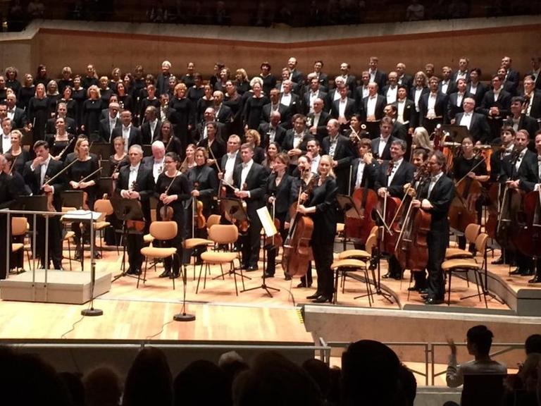 Ein Orchester und ein Chor nehmen mit einem Dirigenten den Beifall des Publikums in der Berliner Philharmonie an.