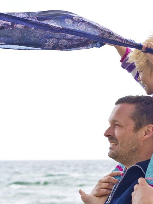 Ein kleines Mädchen und ihr Vater lassen ein Tuch wehen, am Strand von Ringkoebing, Dänemark im Sommer 2014.