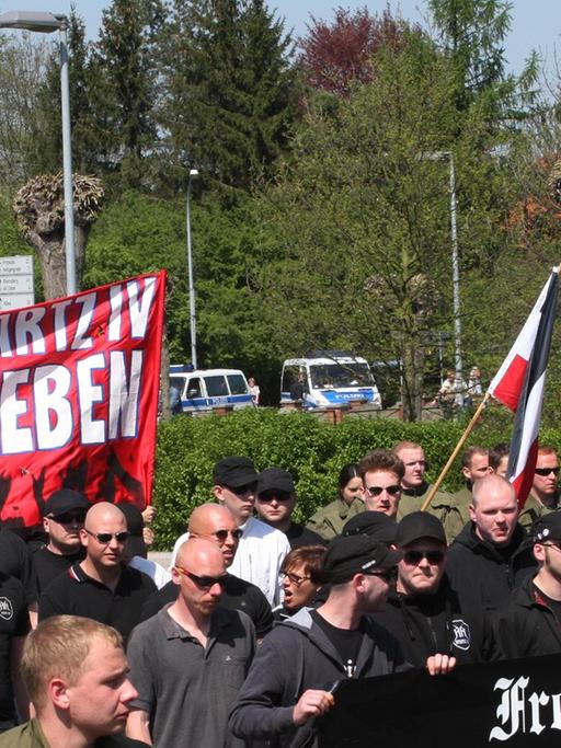 Rund 120 Neonazis laufen in Wittstock (Brandenburg) mit Bannern und Fahnen. Im Hintergrund ist eine Kirche zu sehen.