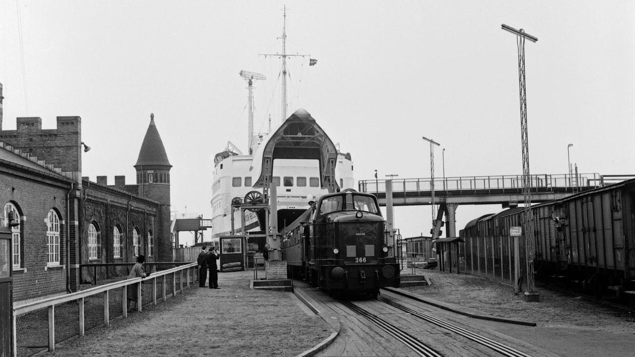 Schwarz-weiß Foto, auf dem ein Zug die Fähre verlässt im Hafen von Puttgarden auf der Insel Fehmarn in den 1960er Jahren.