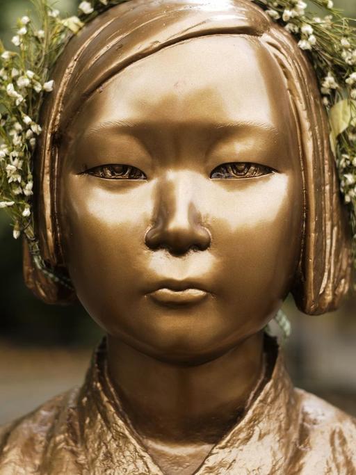 Nahaufnahme der bronzenen Statue eines koreanischen Mädchens mit einem Blumenkranz auf dem Kopf.