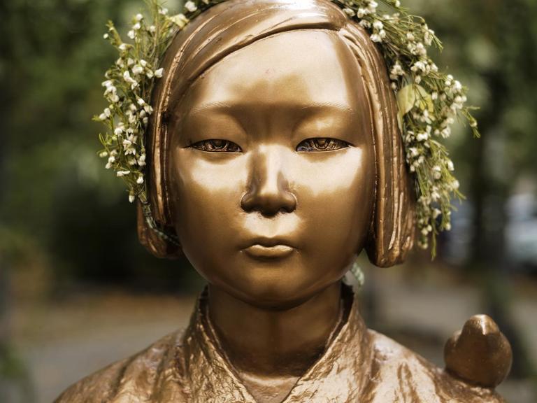 Nahaufnahme der bronzenen Statue eines koreanischen Mädchens mit einem Blumenkranz auf dem Kopf.