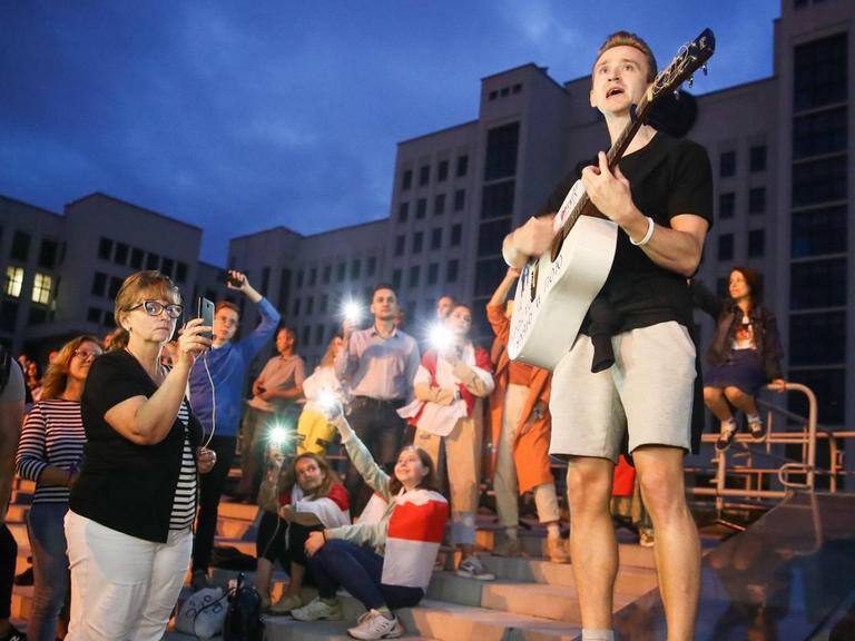 Ein junger Gitarrist gibt in Minsk abends auf einen Platz ein spontanes Konzert. Das Publikum macht Fotos, einige haben sich in die belarusische Fahne gewickelt. Valery Sharifulin/TASS PUBLICATIONxINxGERxAUTxONLY TS0E4073