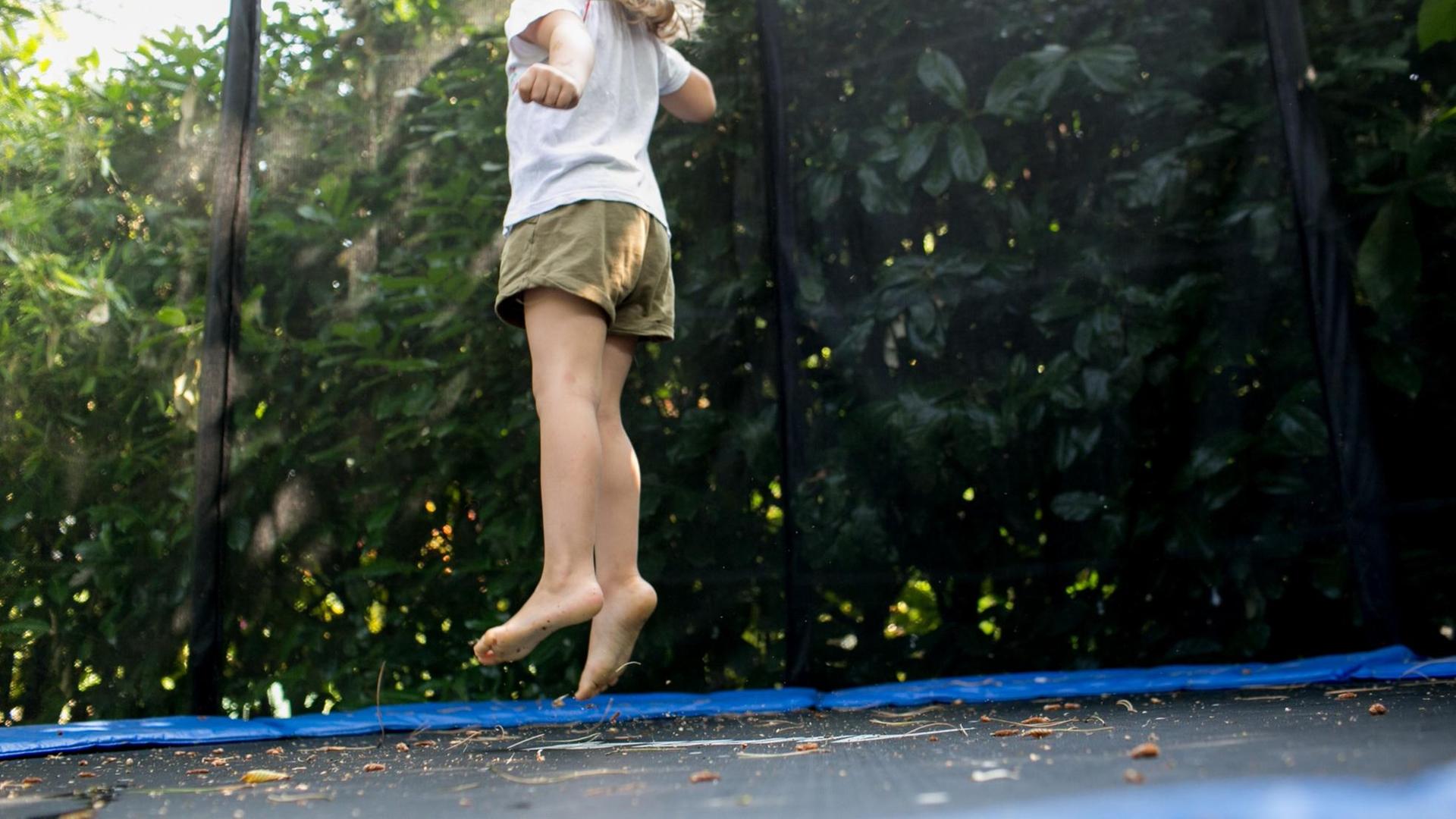 Ein Mädchen springt in einem Garten auf einem Trampolin.