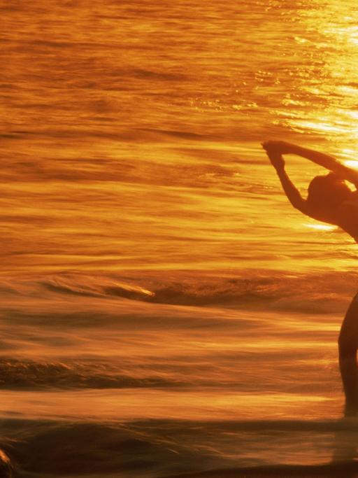 Eine Frau entspannt sich bei Yoga-Übungen im Licht der untergehenden Sonne an einem Strand in Kalifornien.