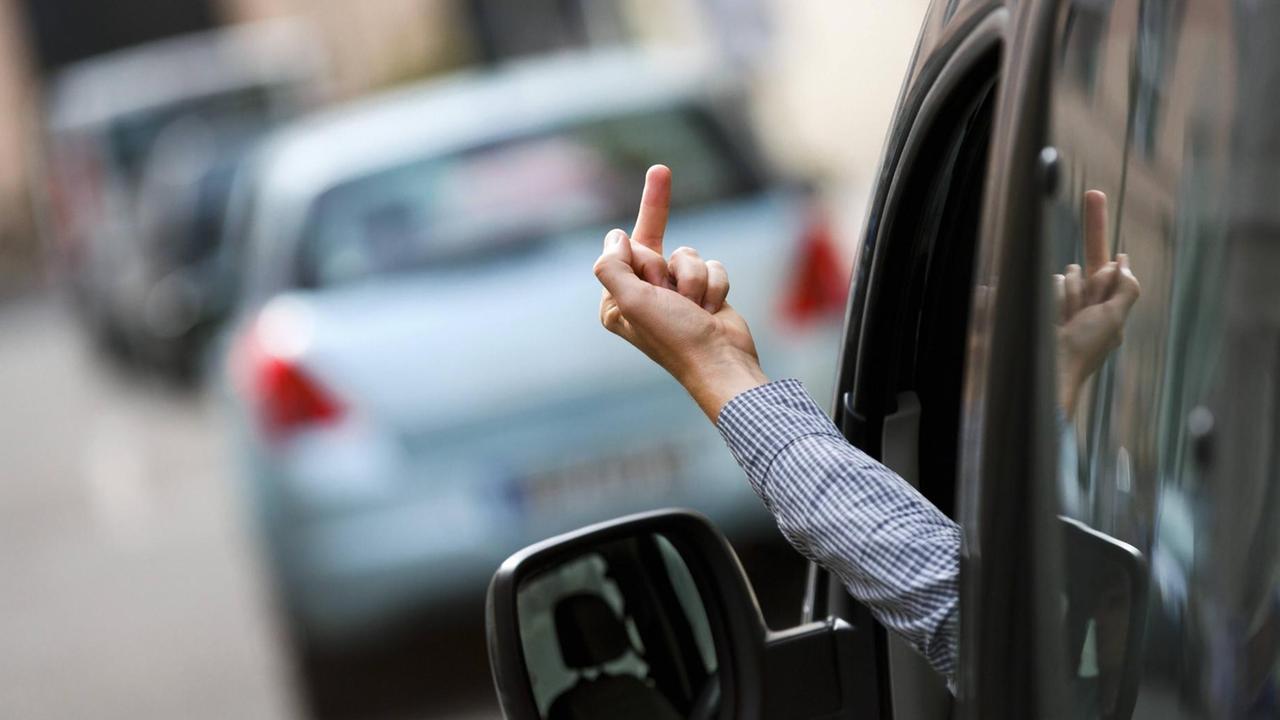 Ein Autofahrer zeigt seinen Mittelfinger einem anderen Verkehrsteilnehmer aus dem Fenster eines Autos.