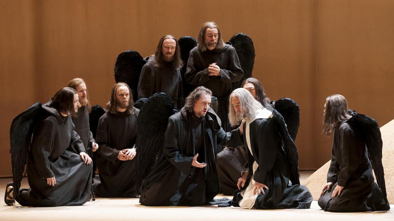 Eine Horde schwarzer Engel mit Jesus ähnlichen langen Haaren und Bärten sitzt eng beieinander auf einer Bühne.