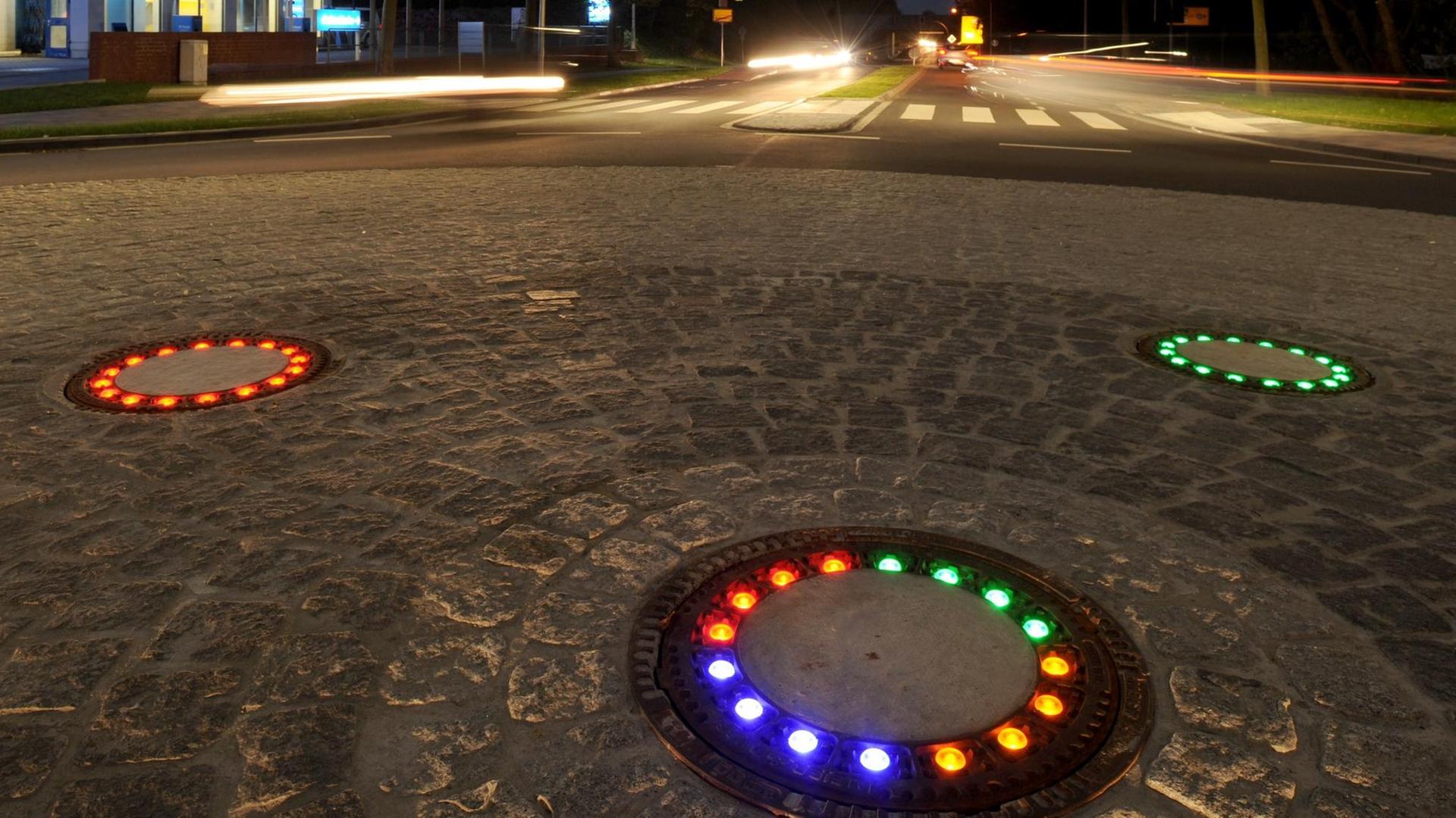 LED-Licht beleuchtet am 22.10.2014 insgesamt fünf Gullydeckel auf einem Verkehrskreisel in Wallenhorst (Niedersachsen)