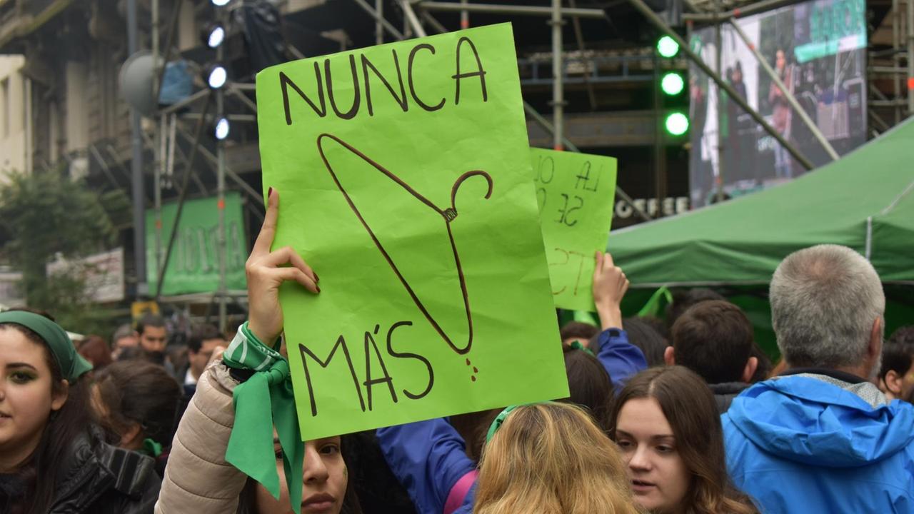 Eine Demonstrantin hält ein Schild in die Höhe, auf dem ein blutiger Kleiderbügel und die Worte "Nunca Mas" ("Nie wieder") zu sehen sind.