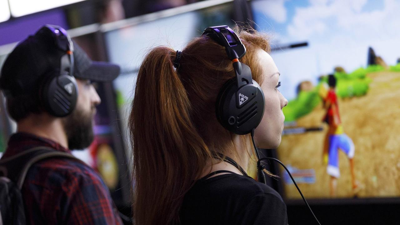 Ein Mann und eine Frau stehen in einer Halle, haben jeweils einen Kopfhörer auf und spielen ein Computerspiel.