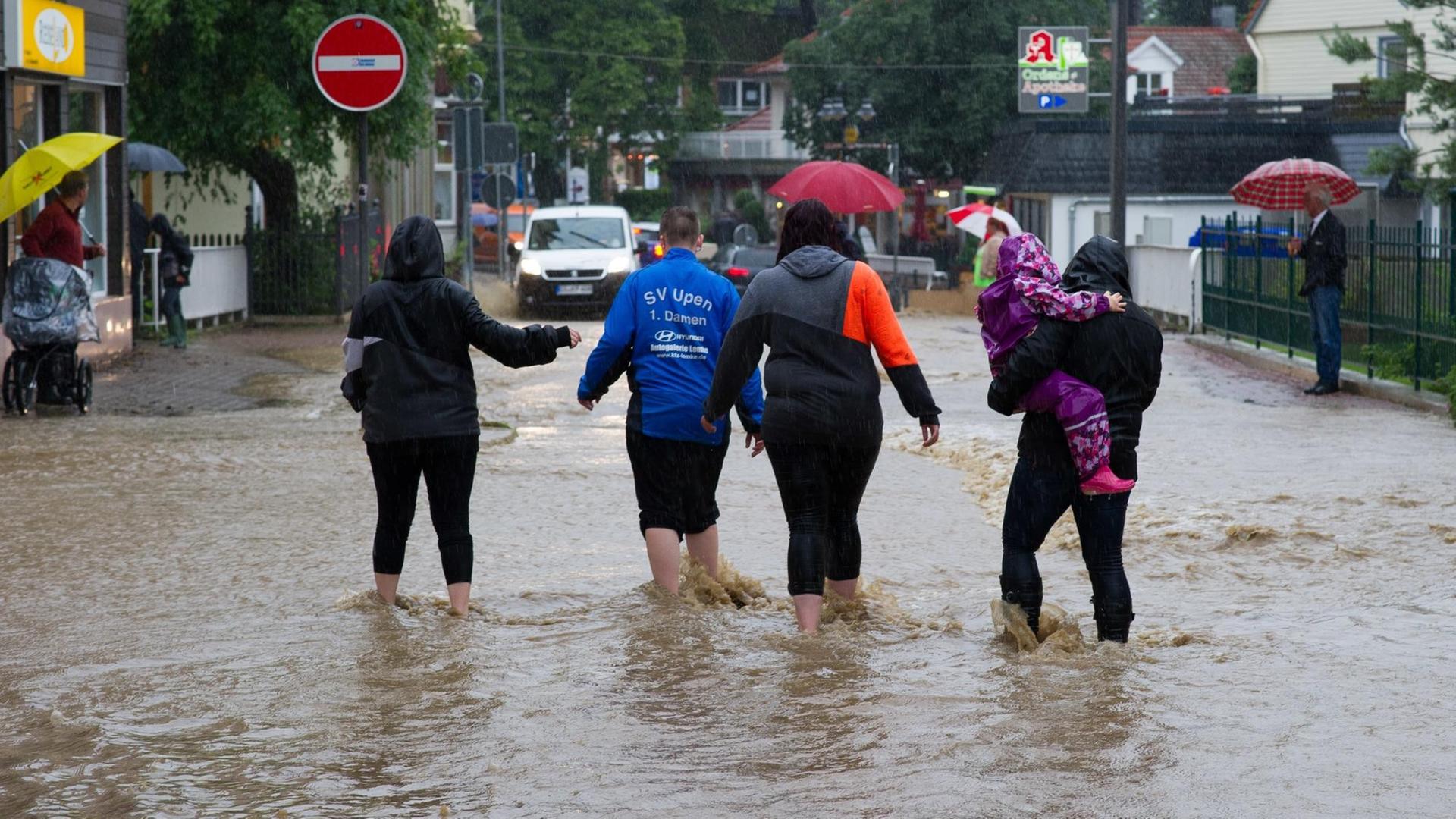 Passanten gehen am 26.07.2017 in Bad Harzburg (Niedersachsen) durch Wasser einer überfluteten Straße. Dauerregen hat im südlichen Niedersachsen in einigen Orten zu Überschwemmungen geführt.