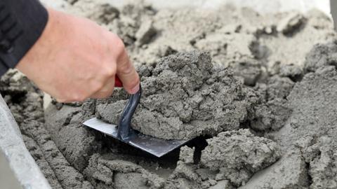 Mit einer Maurerkelle hebt ein Mann Mörtel.
