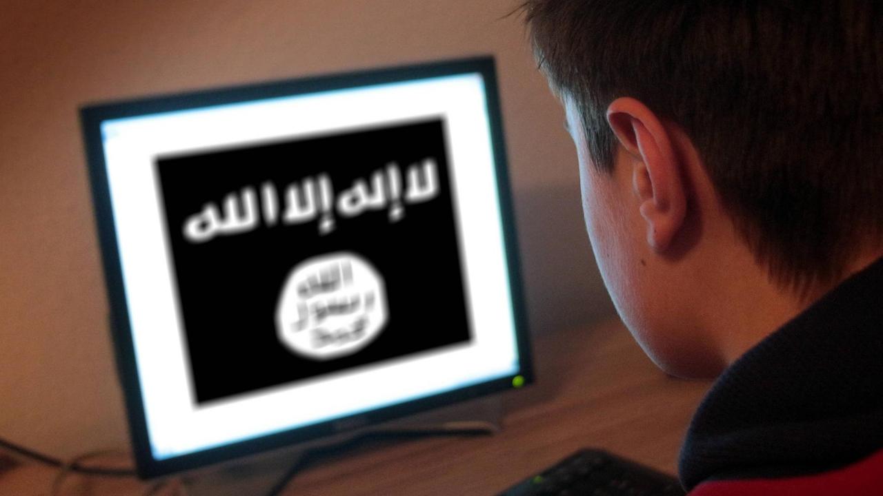Ein Jugendlicher sitzt am Bildschirm eines PCs, der die Flagge der Terrormiliz IS zeigt.