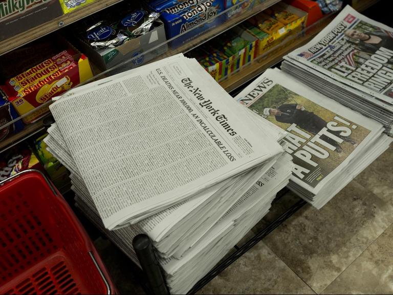 Zeitungsstapel in einem New Yorker Kiosk, darunter die New York Times und die New York Post.