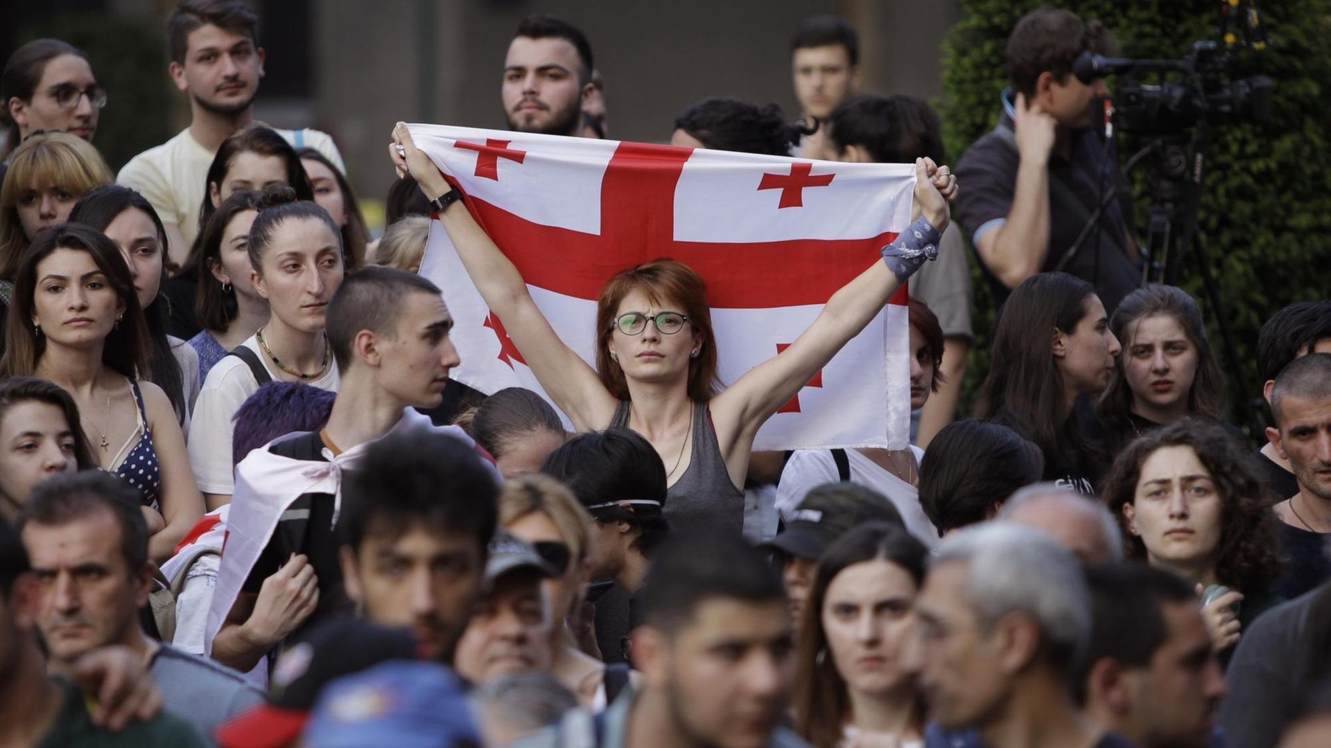 Im Zentrum der Menschenmenge steht eine Frau mit Brille, die eine georgische Flagge hochhält.