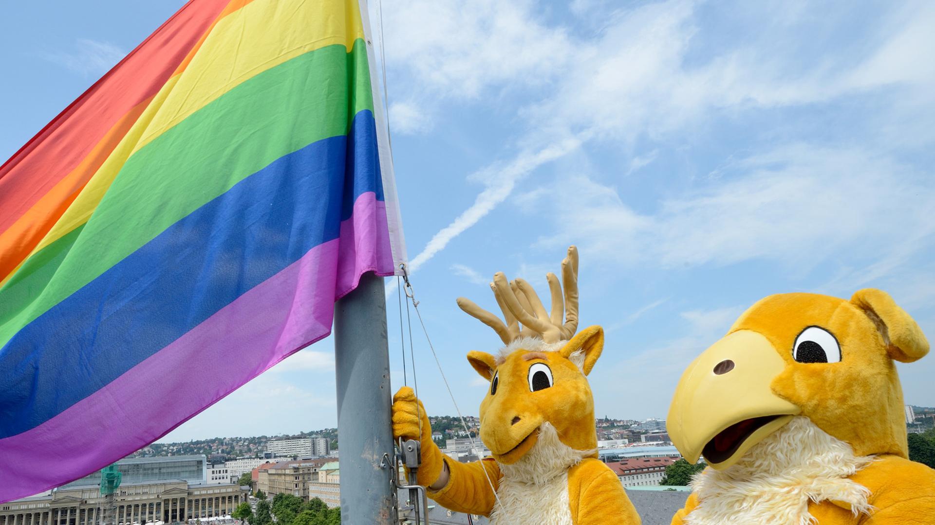 Zwei Menschen in Ganzkörperkostümen der Wappenfiguren des Landes Baden-Württemberg, Hirsch und Greif, hissen auf der Kuppel des Neuen Schlosses in Stuttgart die Regenbogenfahne, das Symbol der Schwulen- und Lesbenbewegung.