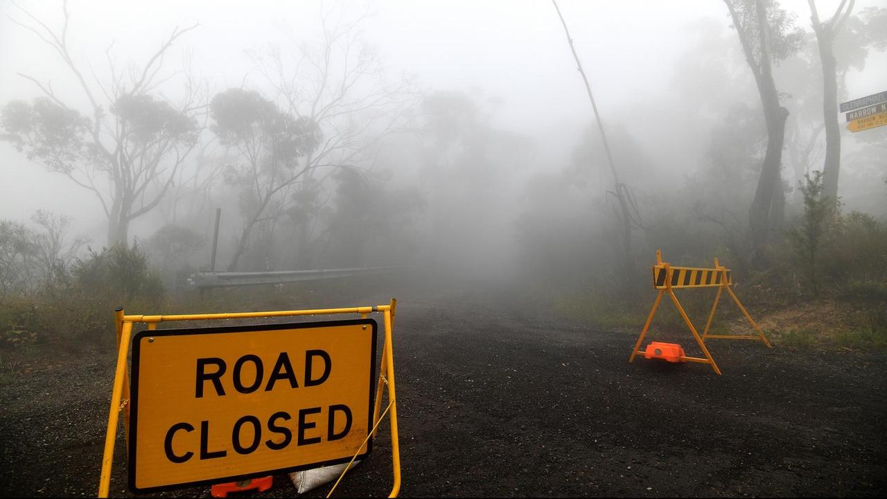 Nebel und Rauch von den Waldbränden verdunkeln in der australischen Region Blue Mountains die Sicht. Schilder weisen auf eine Straßensperrung hin.
