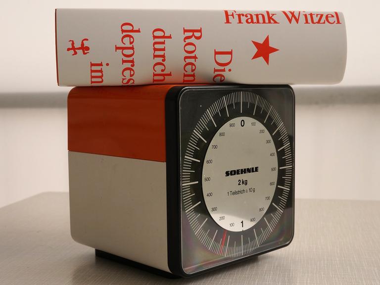 Der Roman "Die Erfindung der Roten Armee Fraktion durch einen manisch-depressiven Teenager im Sommer 1969" von Frank Witzel liegt auf einer Küchenwaage, die etwa 1100 Gramm anzeigt.
