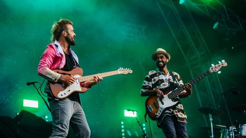 Zwei Männer stehen auf einer Bühne, der linke spielt E-Gitarre, der rechte einen fünfsaitigen E-Bass.