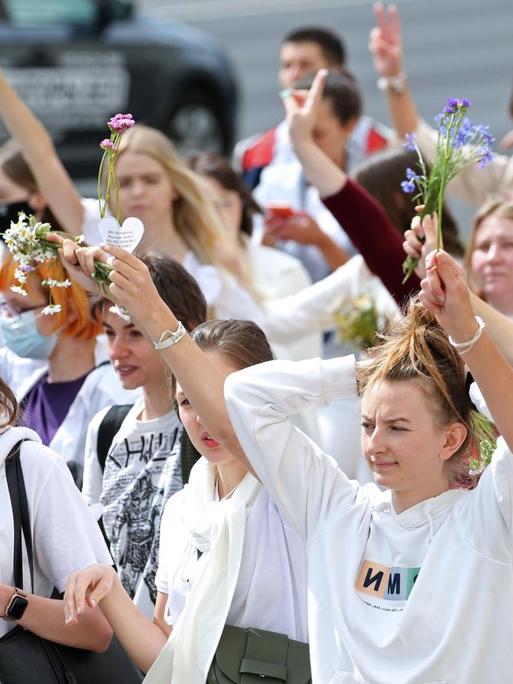 Junge Frauen demonstrieren. Sie tragen weiße Kleidung und halten Blumen in den Händen.