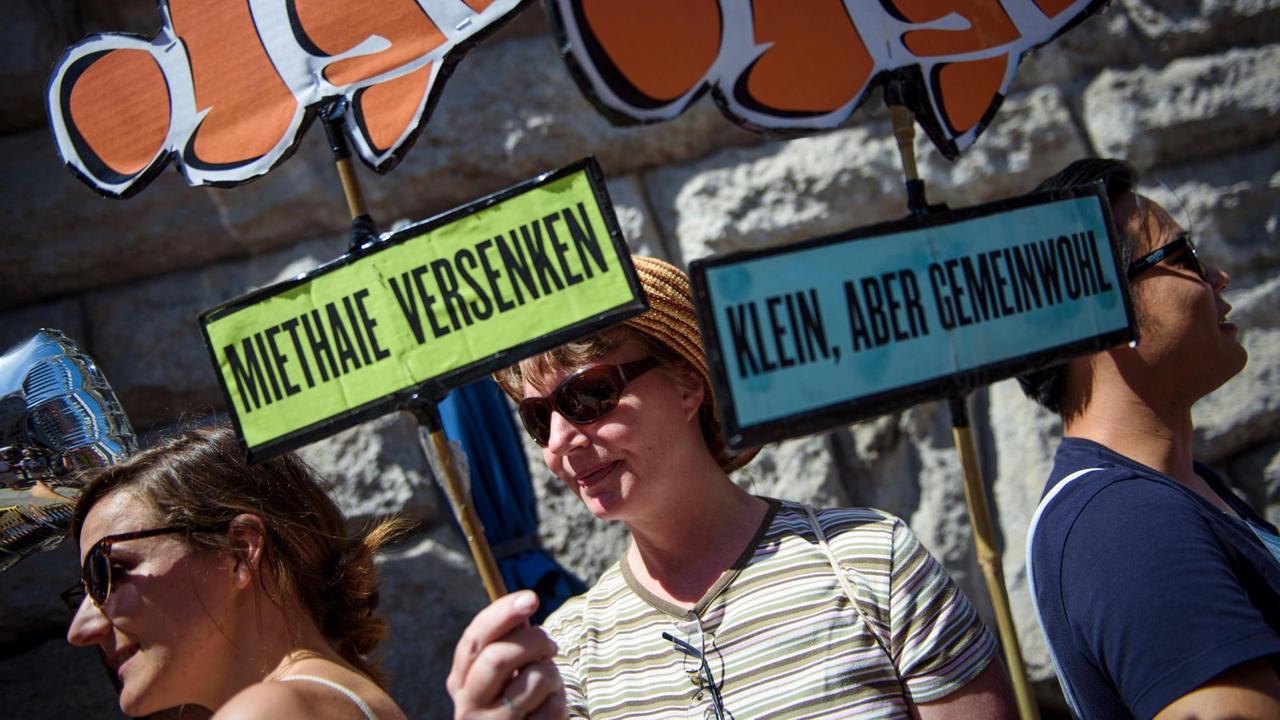 Eine Aktivistin der Initiative "Deutsche Wohnen & Co enteignen" nimmt mit selbstgebastelten Schildern, afu dem "Miethaie versenken" und "Klein, aber Gemeinwohl" steht, an der Übergabe von 77.001 Unterschriften zur Anstrebung eines Volksbegehrens an die Berliner Senatsverwaltung für Inneres und Sport teil.