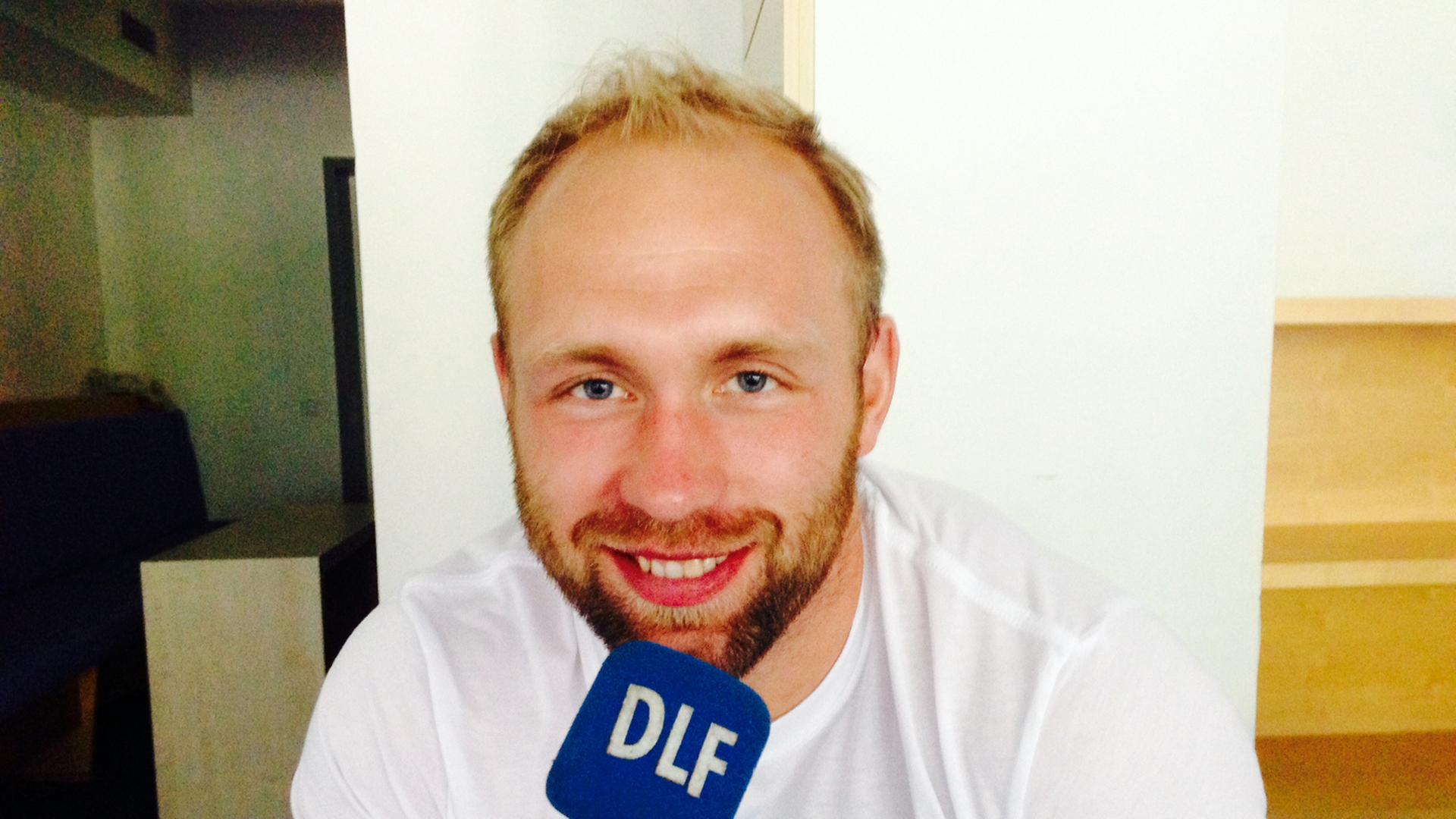 Diskus-Olympia-Sieger Robert Harting hält ein Mikrofon mit der Aufschrift DLF in der Hand.