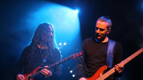 Zwei Männer an Bass und Gitarre stehen auf einer in blaues Licht getauchten Bühne. 