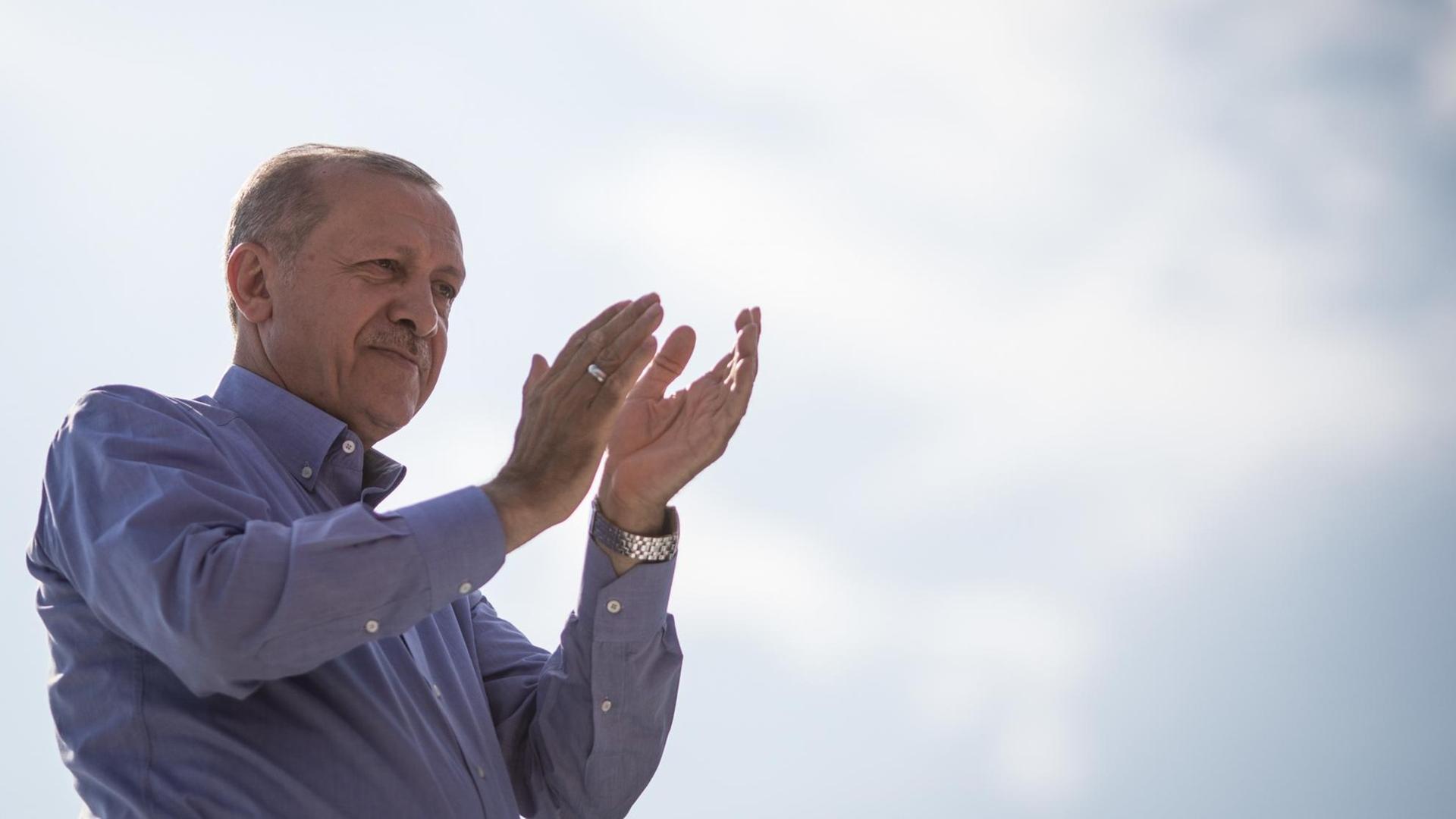 Der türkische Präsident Erdogan in blauen Hemd klatschend vor blau-weißem Himmel.