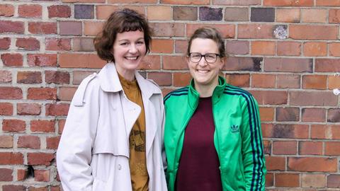 Die Regisseurin Eva-Maria Baumeister und die Stadtplanerin Isabel Finkenberger stehen vor einer Backsteinmauer.