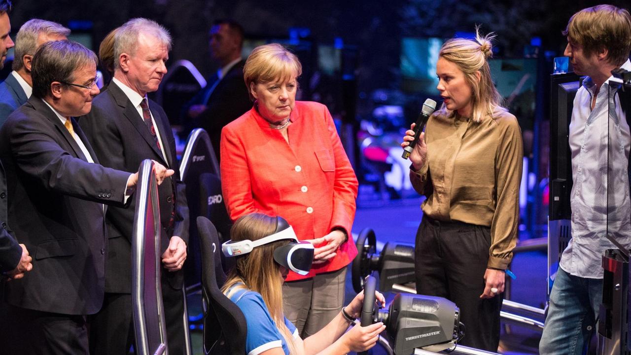 Bundeskanzlerin Angela Merkel schaut auf der Gamescom in Köln ein virtuelles Autorenn-Computerspiel an.