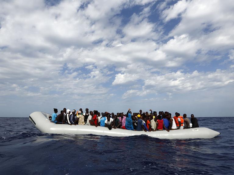 Vor der Insel Lampedusa warten Flüchtlinge in einem Schlauchboot darauf, in Sicherheit gebracht zu werden.
