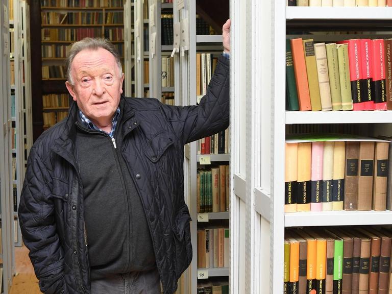 Peter Sodann steht inmitten von Buchregalen seiner Sammlung von Büchern, die in der DDR erschienen sind.