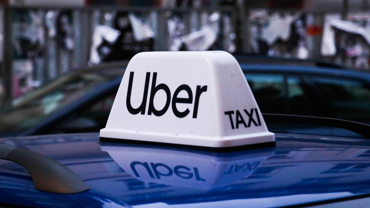 Ein Auto trägt auf dem Dach ein Uber Zeichen, an dem auf der Seite "Taxi" zu lesen ist. 