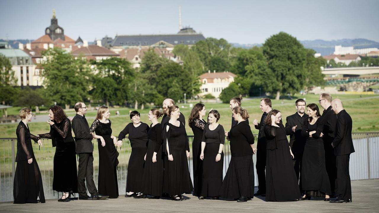 Der Chor steht in seiner schwarzen Kleidung auf einer Terrasse nahe der Elbe in Dresden.
