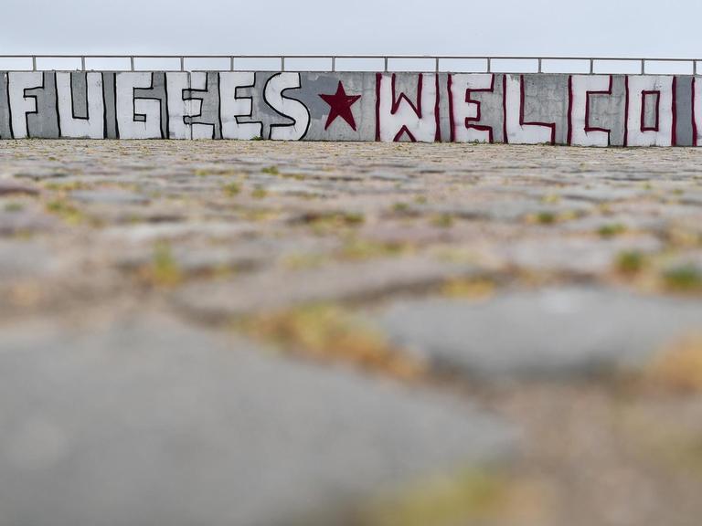 In großen Buchstaben steht auf Englisch "Refugees Welcome" (Flüchtlinge willkommen) am 25.05.2016 an einer Mauer am Ufer der Oder in Frankfurt (Oder) (Brandenburg).