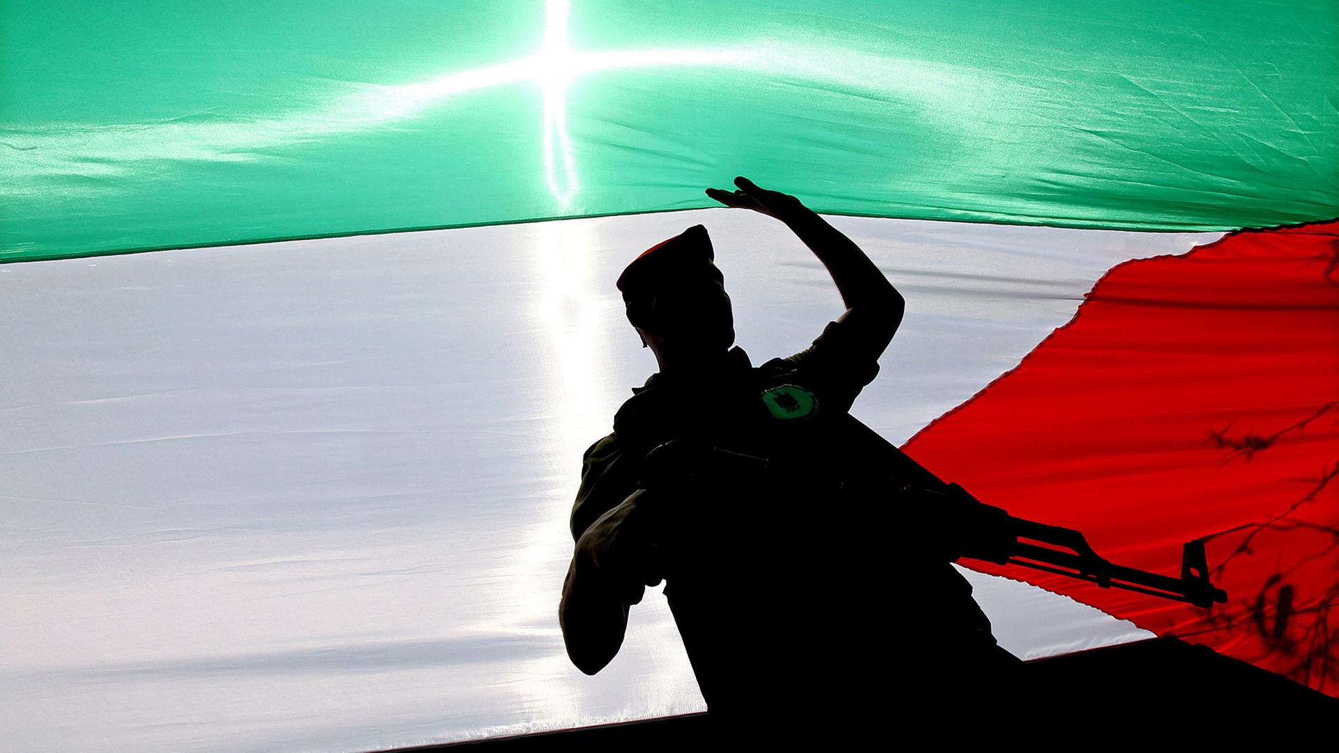 Ein bewaffneter Hamas-Aktivist läuft in Gaza-Stadt unter einer Palästinenser-Flagge.