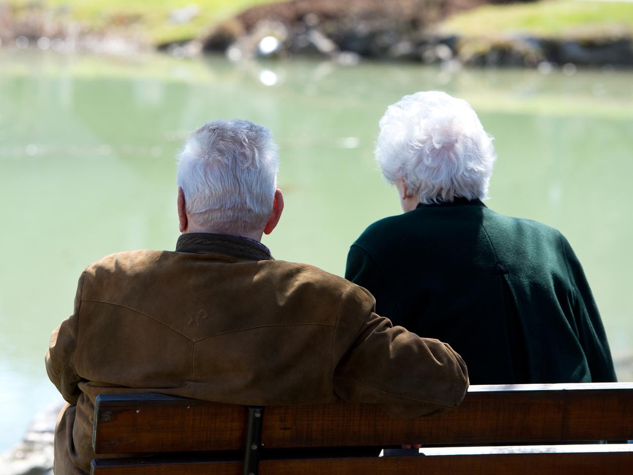 Zwei Senioren sitzen an einem kleinen Teich.