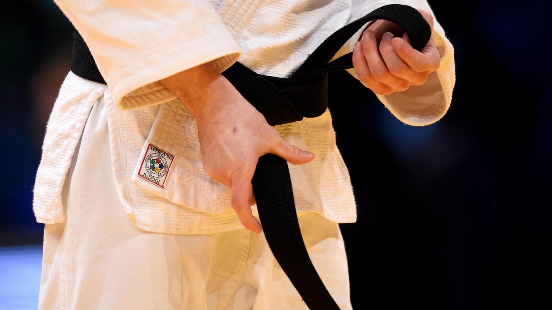 Hände binden einen Judo-Gurt. Man kann nicht erkennen, wer das ist. Es ist ein Symbol-Foto. 