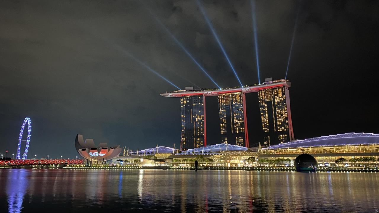 Drei Hochhäuser stehen  vor einem Gewässer bei Nacht und werden spekakulär beleuchtet.
