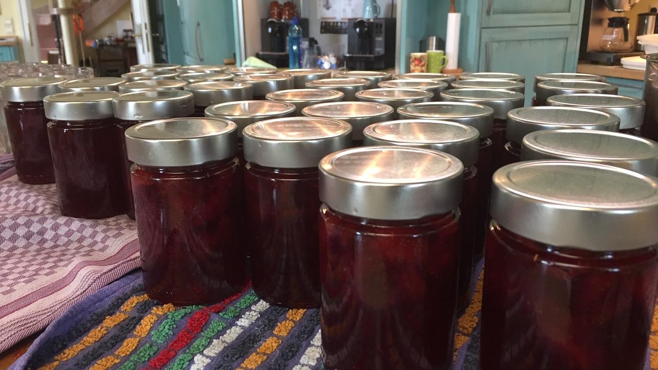 Dutzende Gläser mit Erdbeermarmelade stehen in einer Küche. Die Gläser haben kein Etikett. 