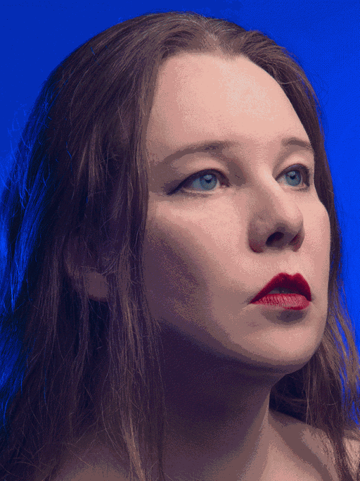 Porträt der Sängerin mit dunklen, langen, offenen Haaren vor blauem Hintergrund.