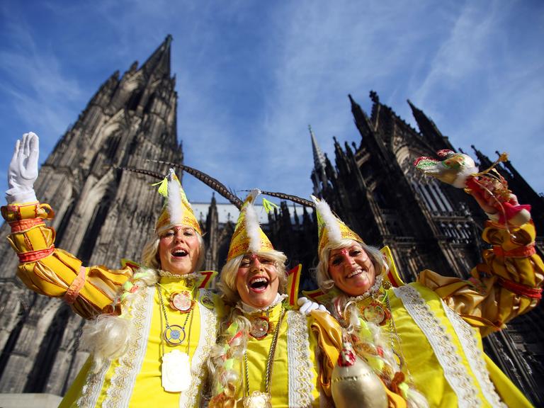 Drei Karnevalistinnen aus Holland in gelben Kostümen winken am 27.02.2014 zur Weiberfastnacht in Köln (Nordrhein-Westfalen) vor dem Kölner Dom.