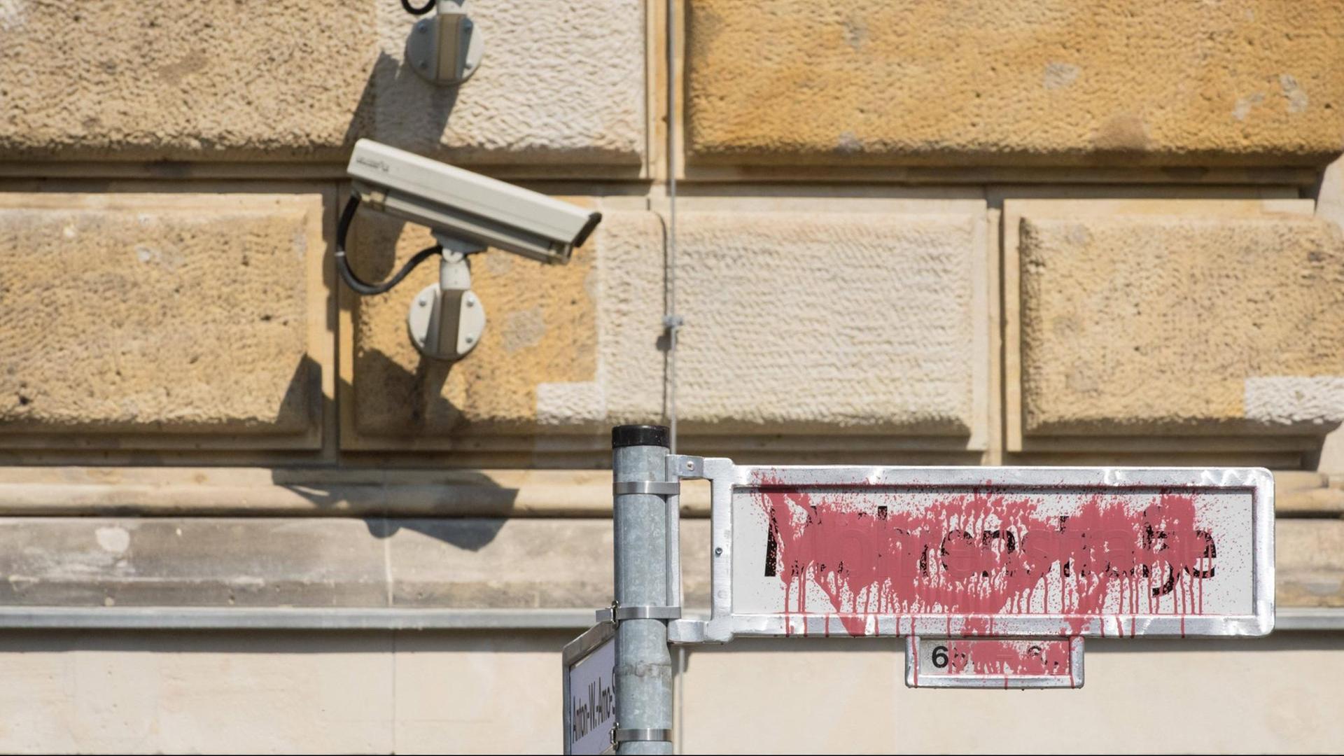 Im Bild ist das mit rote Farbe besprühte Straßenschild Mohrenstraße zu sehen. Darüber hängt an einer Hauswand eine Überwachungskamera.