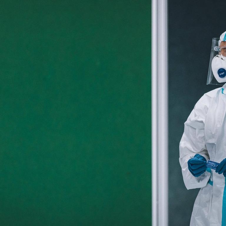 Eine Frau in einem Schutzanzug steht am 05.12.2020 in einer Coronvirus-Teststation in Saalfelden, Österreich, vor einer grünen Wand