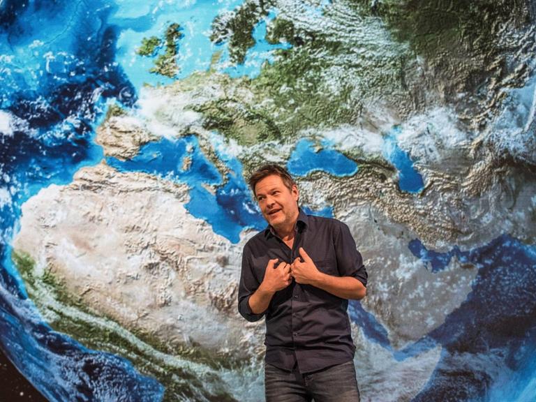 Robert Habeck steht auf einer Bühne, hinter ihm ein riesiges Bild der Weltkugel