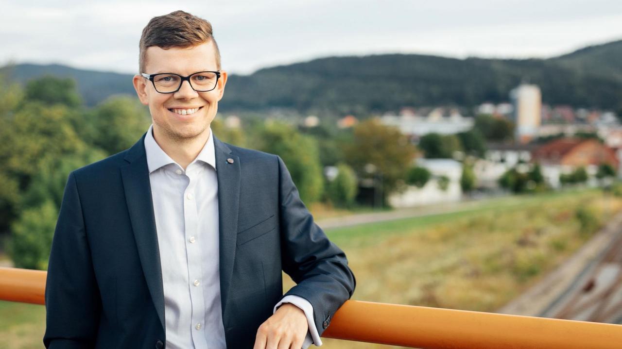 Daniel Schultheiß, Oberbürgermeister von Ilmenau, lehnt an einem Geländer. Im Hintergrund ist Ilmenau zu sehen.