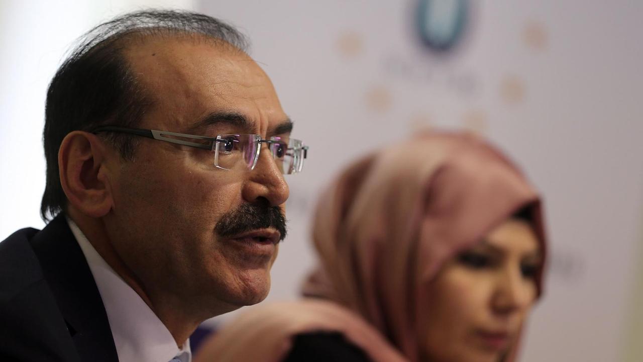 Süleyman Celik, ehemaliger Vorsitzender der Union europäisch-türkischer Demokraten, sprechend, im Hintergrund unscharf sitzt eine Frau mit Kopftuch