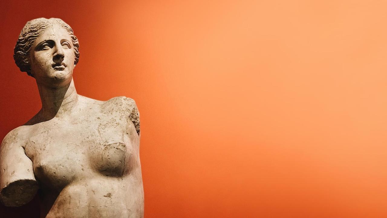 Der Torso einer antiken Frauenstatue vor einem orangefarbenen Hintergrund.